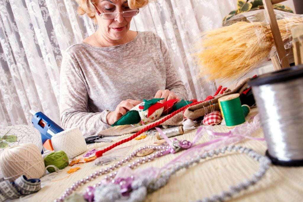 Senior woman sews by hand while making an owl ornament