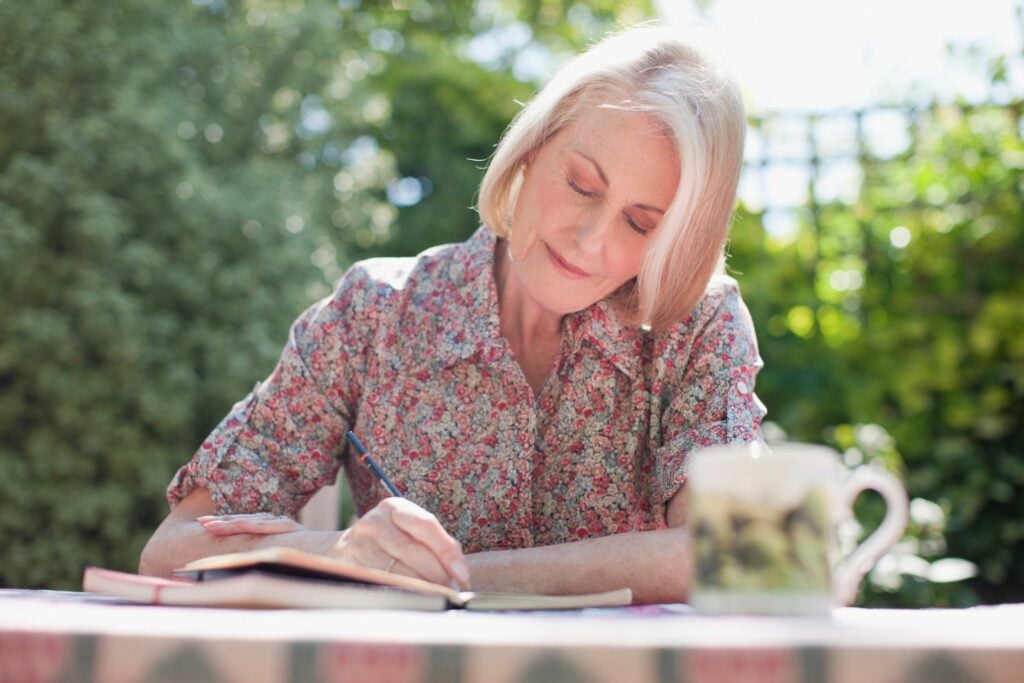 Older woman writing in a journal at a patio table