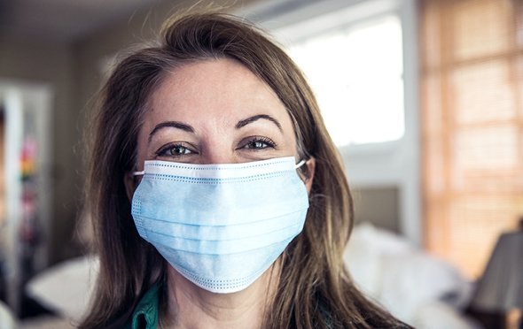 Caregiver with smiling eyes indoors wearing a medical mask.
