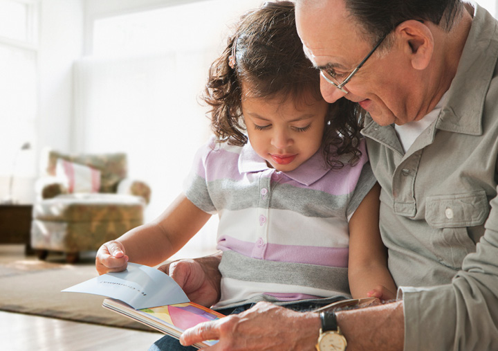 Grandpa reading a book to a young granddaughter sitting in his lap.