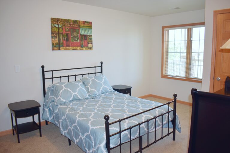 senior living apartment bedroom with a bed, side tables, dresser, closet and window in Green Bay