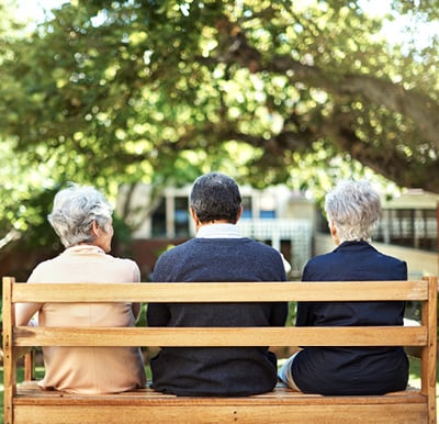 Three friends sitting on a bench in a landscaped courtyard with large trees.