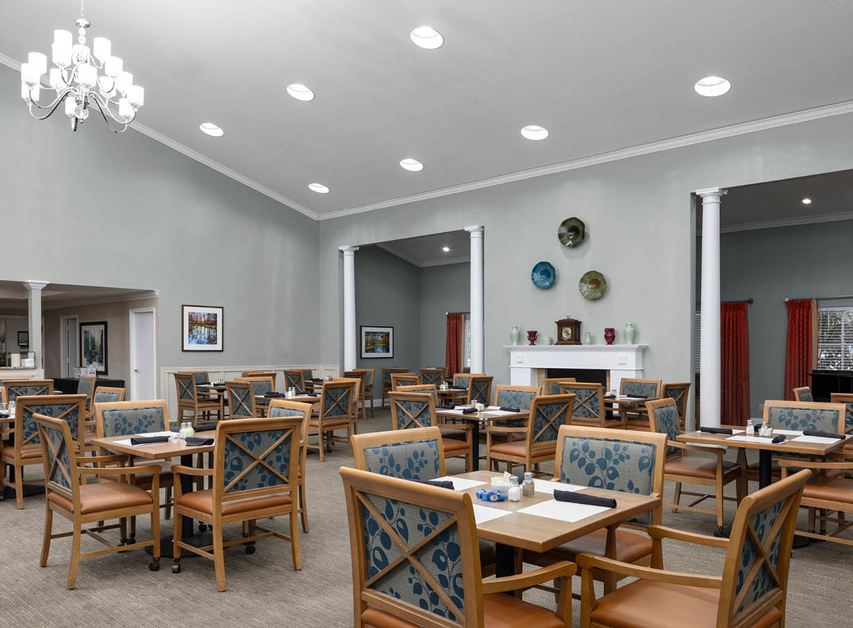 Elegant and spacious dining room with many tables and chairs, chandeliers and a fireplace at senior living community in Mesquite, Texas