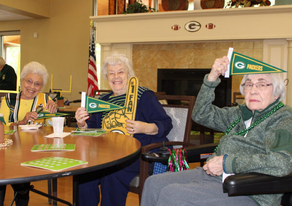 Three senior women smile and cheer for the Green Bay Packers at Brookview Meadows, a senior living community