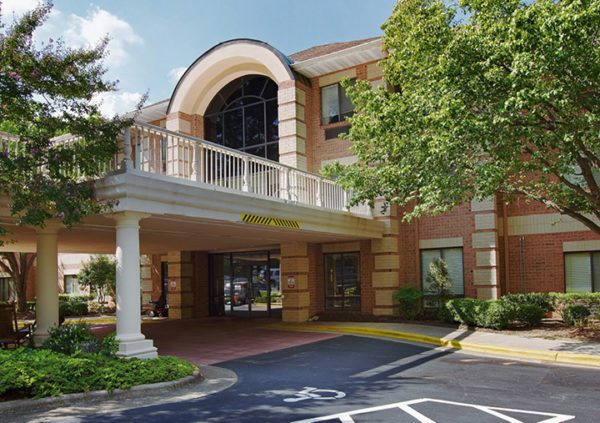 The outside of a senior living community in Raleigh, NC with brick exterior, portico entrance and trees.