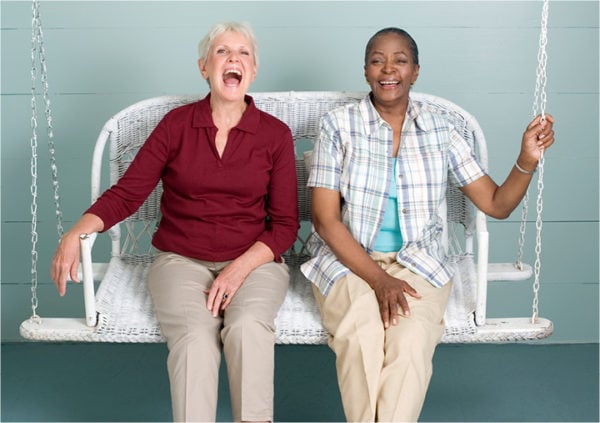 Two women laughing and swinging together on a porch swing