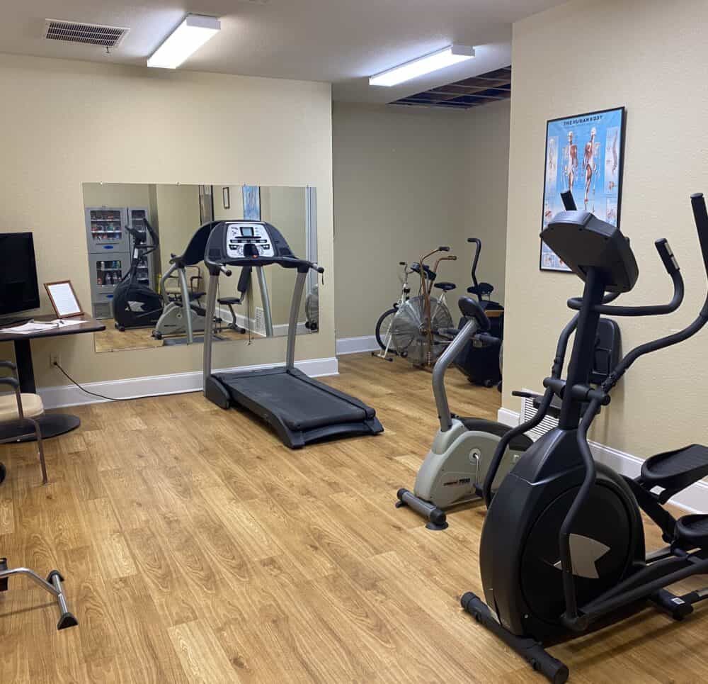 Exercise room at a senior living community in Mesquite, Texas with exercise machines and free weights.