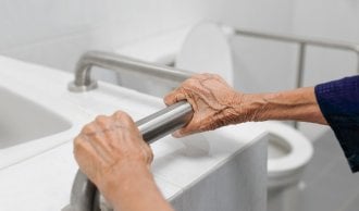 Senior woman holds onto rail bar in a bathroom for safety.