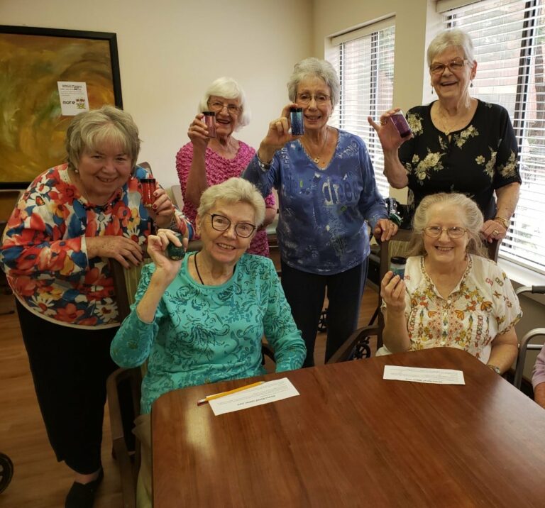 Group of senior women smile and show off their new craft project at a senior living community in Raleigh, North Carolina.