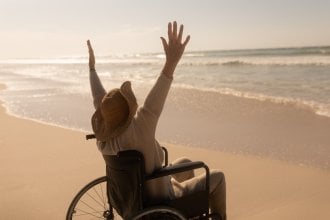 Senior embraces the warmth and waves while in a wheelchair at the beach.