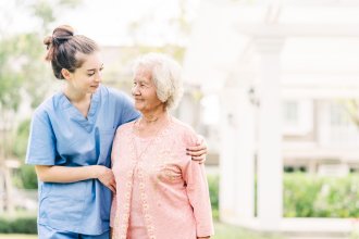 Young caregiver woman embraces senior woman while on a walk.