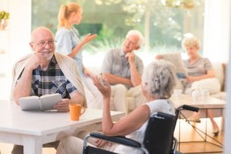 Senior friends laugh and smile while interacting with each other in senior living setting.