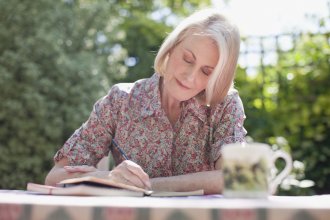 Senior woman journals in a notebook in an outdoor courtyard.