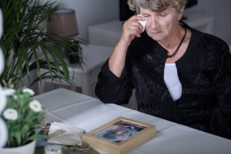 Senior woman wipes away a tear while looking at a picture of a senior man.