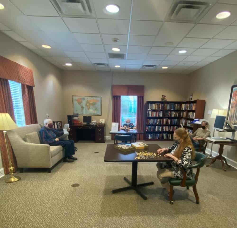 Seniors relaxing on a couch and another woman solves a puzzle at a table at a senior living community located in Richardson, Texas.