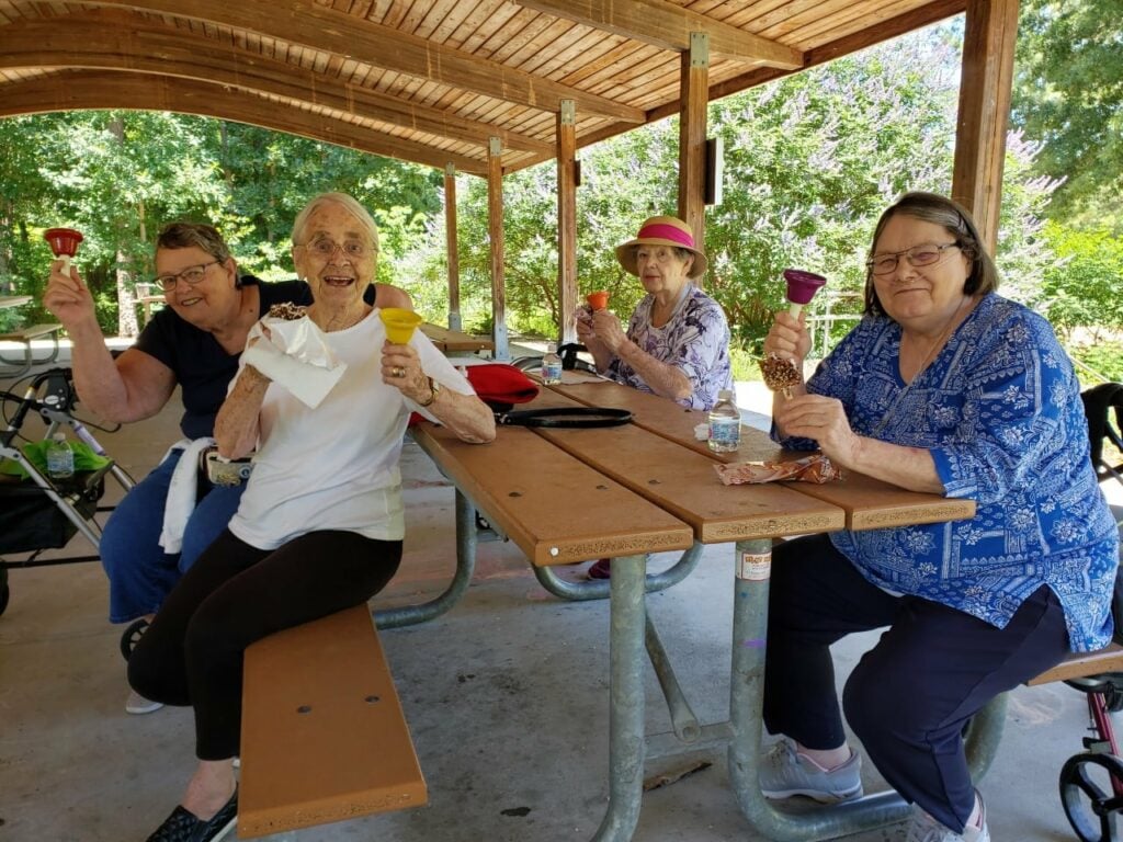 Four senior women smile with their bells while sitting at a park at a senior living community in Raleigh, North Carolina.