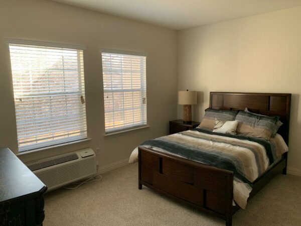bedroom with a queen-sized bed, side table and lamp near two windows