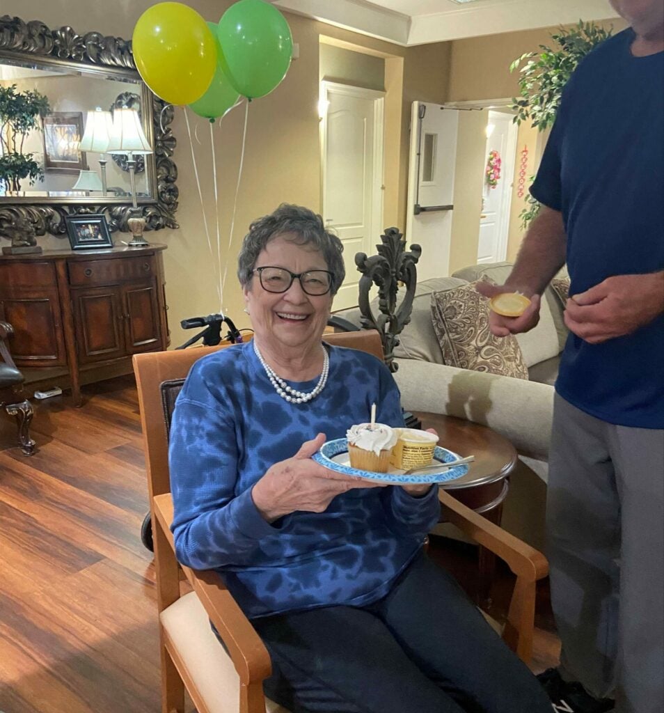 Senior woman holds up cupcake during birthday party at a senior living community in Arlington, Texas.