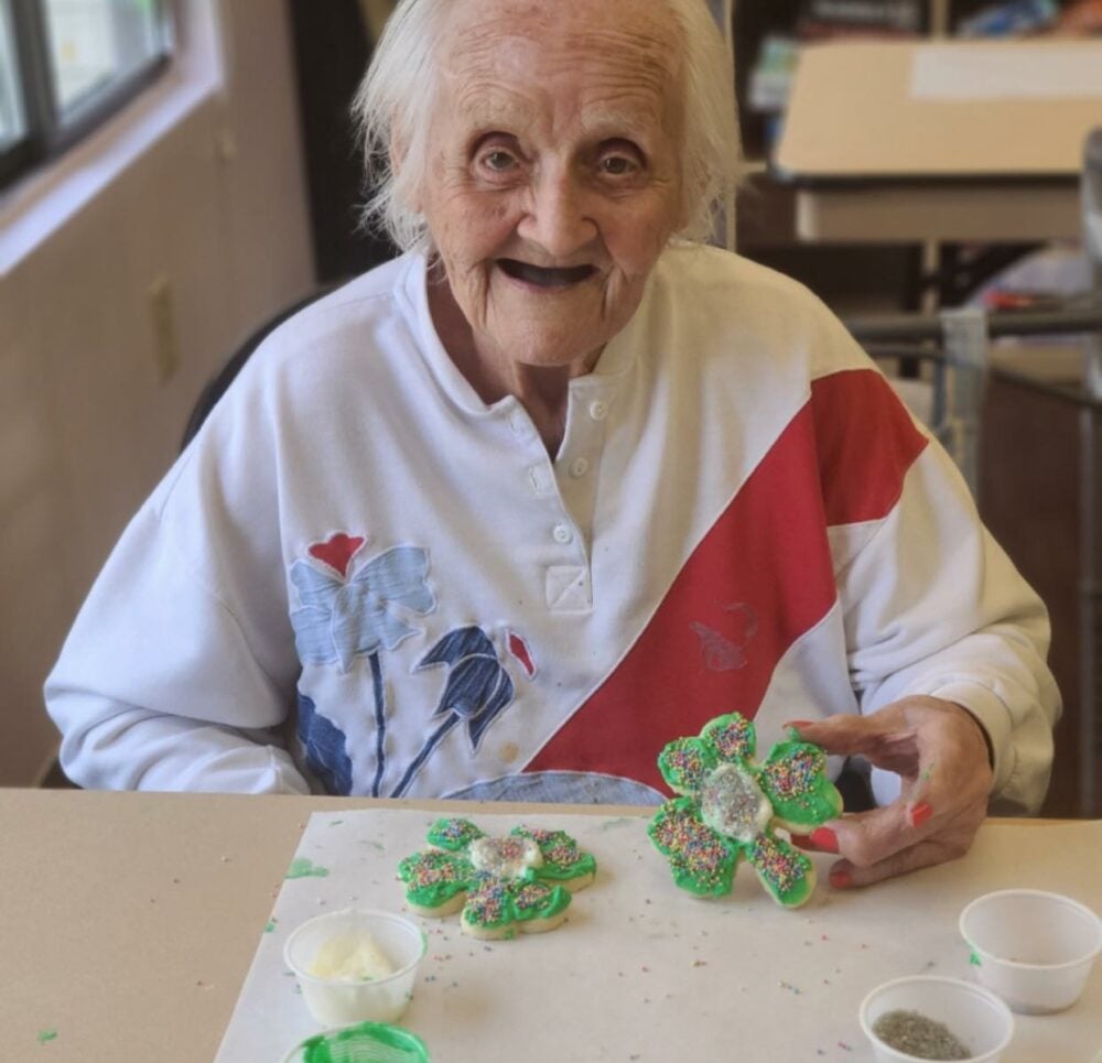 senior woman smiles with her decorated shamrock cookie
