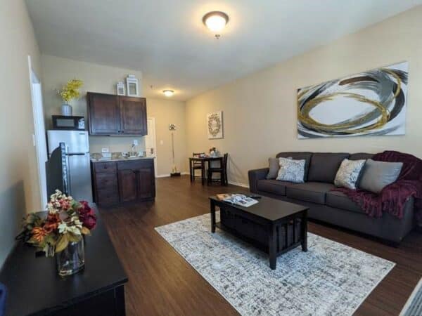 Apartment living room and kitchen with couch, refrigerator and sink at a senior living facility in San Antonio, Texas.