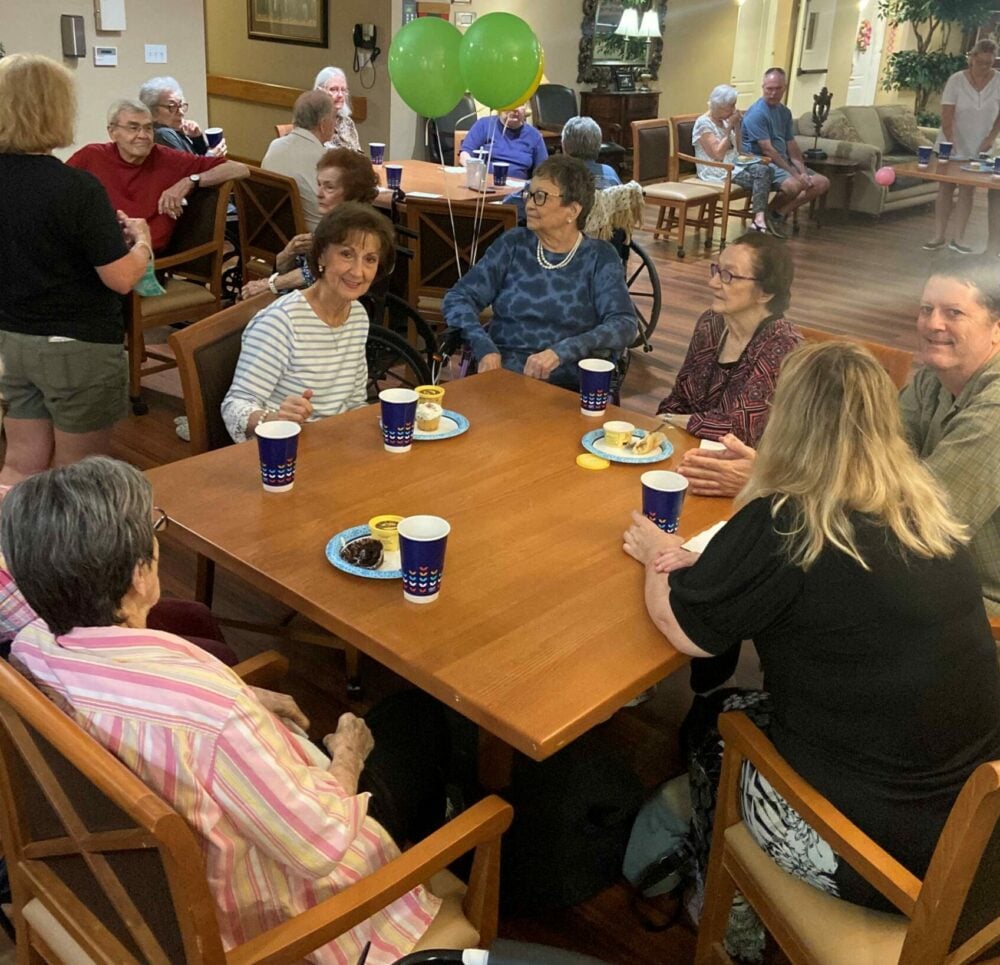 Seniors gather around a table with birthday treats at a senior living community in Arlington, Texas.