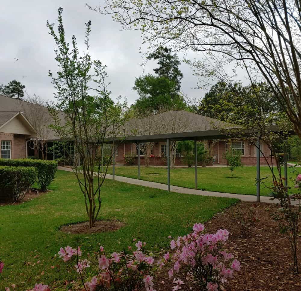 Outdoor courtyard at senior living facility with walking path and trees in Conroe, Texas.