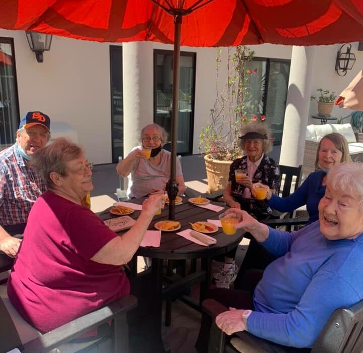 group of seniors smile and cheers together outside on a patio