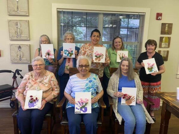 Eight women take a group shot together holding up their artwork at a senior living community in Stephenville, Texas.