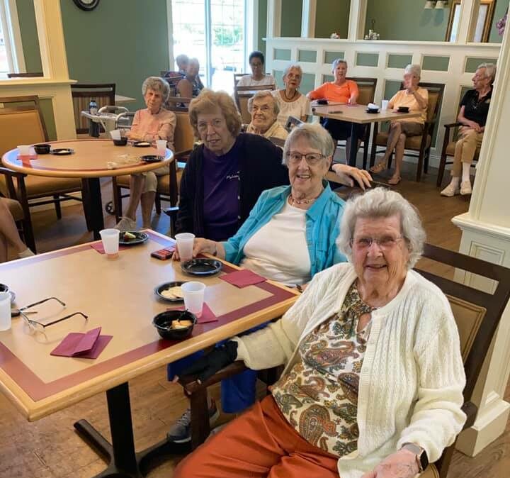 three senior women smile while enjoying food and a musical performance