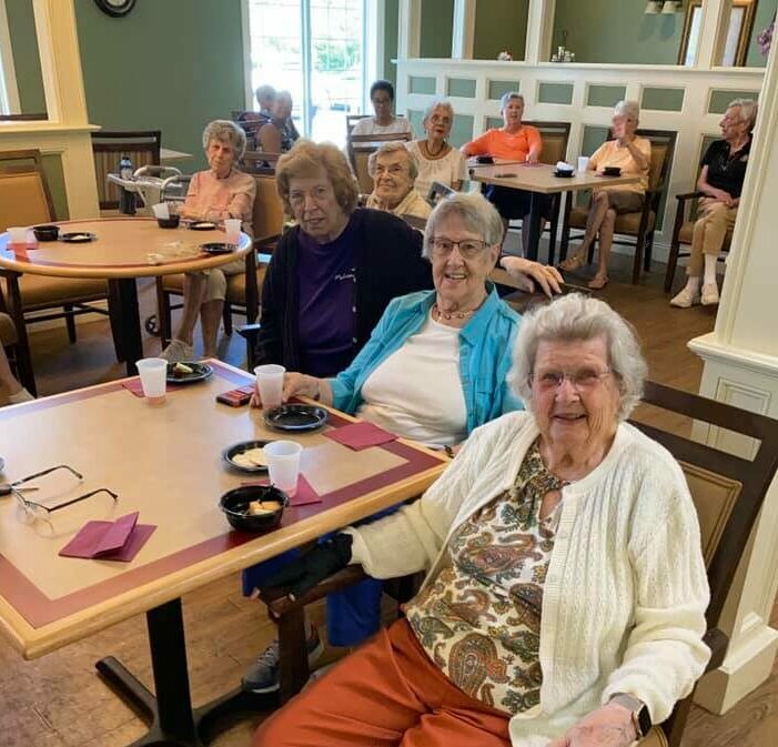 three senior women smile while enjoying food and a musical performance