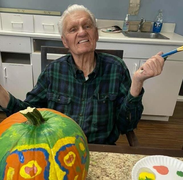 senior man smiles while painting a pumpkin
