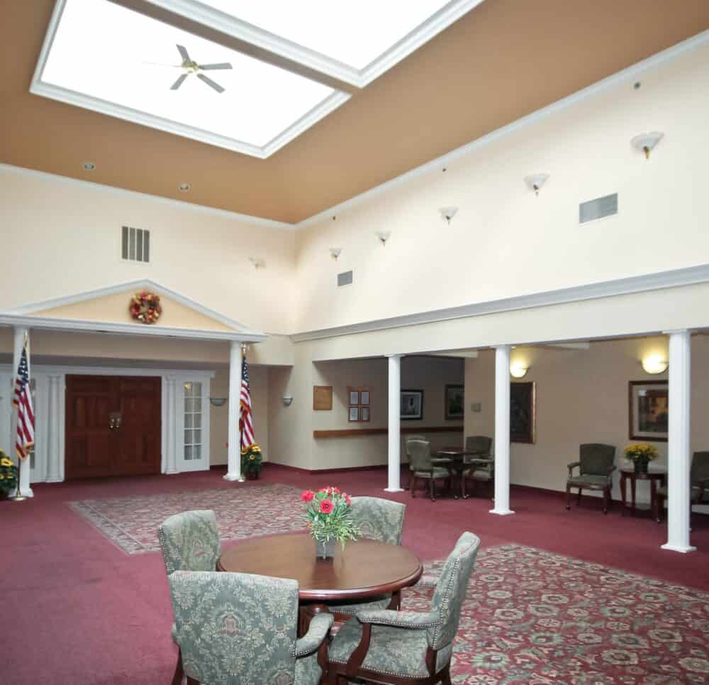 Lobby and lounge area at a senior living facility complete with table and chairs and large ceilings in Williamsville, New York.