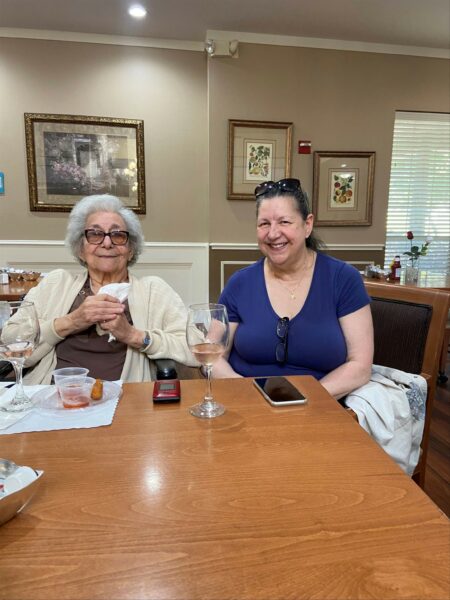 Senior woman and younger woman smile at the camera while sitting next to each other at a senior living community in Arlington, Texas.