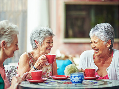 Laughing senior women enjoying coffee on a restaurant patio.