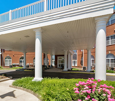 Gorgeous entrance to senior living facility in Macedonia, Ohio with lush landscaping, covered driveway and white columns.