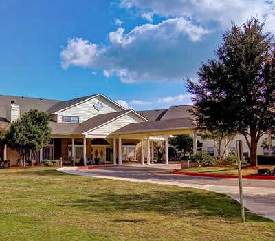 Entrance to senior living community in San Antonio, Texas with manicured lawns and covered driveway.