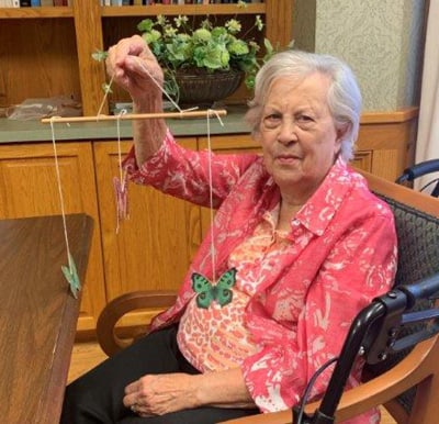 A smiling woman holding up a completed mobile craft in the activity center in Lambertville, Michigan.