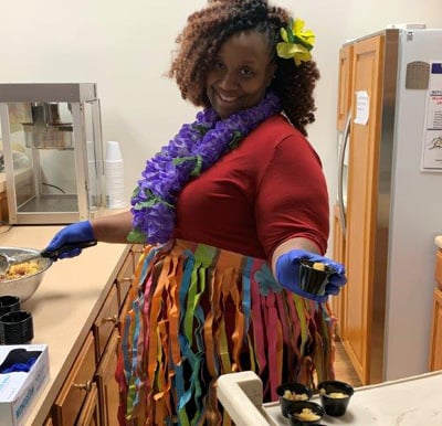 Senior living worker in Lambertville, Michigan wearing a Hawaiian outfit while serving food.