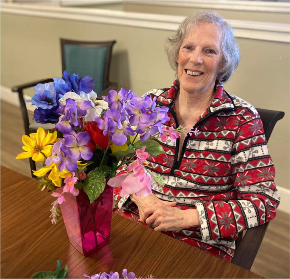 Senior woman smiles with her vace of flowers at a senior living community in Lambertville, Michigan
