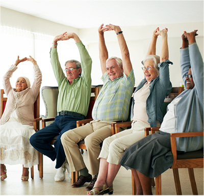 A group of seniors stretching their arms overhead during a chair yoga class.