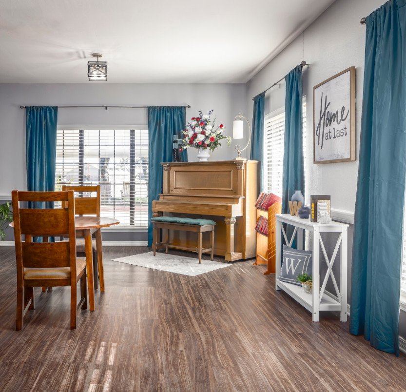 The Waterford at College Station lounge includes a piano, a table with two chairs and windows with views of the College Station area