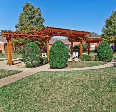 A senior living community courtyard with walking path and a pergola-covered seating area in Arlington, Texas.