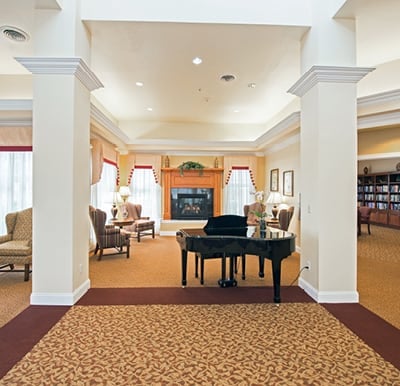 Grand space with columns, a grand piano, a fireplace, lounge seating and French doors opening to a well-stocked library in Dayton, Ohio.