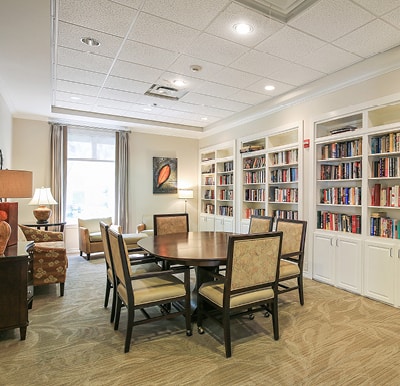 Well-lit library with a wall of bookshelves, a table with chairs in the center of the room and comfortable seating spread around in Ridgeland, Mississippi.
