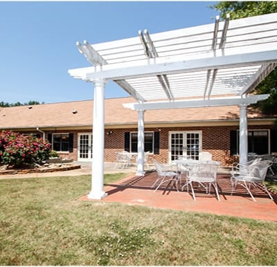 A beautiful, white pergola with outdoor dining furniture in a well-manicured courtyard in Anderson, South Carolina.
