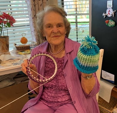 A woman smiling and holding up a hat that she created on a loom in Humble, Texas.