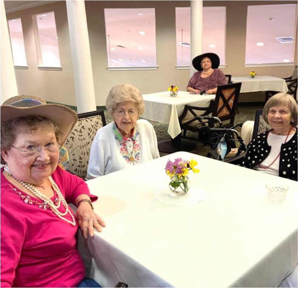 Three senior women smile while seated at a table in an independent living community