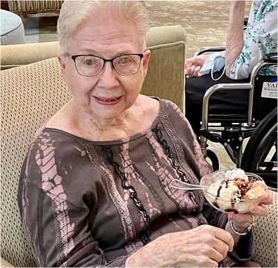 senior woman smiles while holding an ice cream sundae in her hand