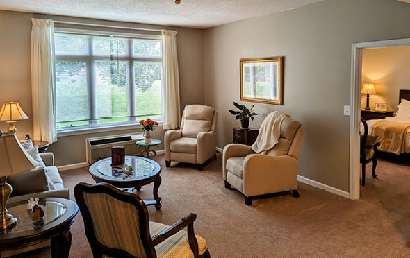 Senior apartment living room with a couch, three chairs, a table and a large window in Greencastle, IN
