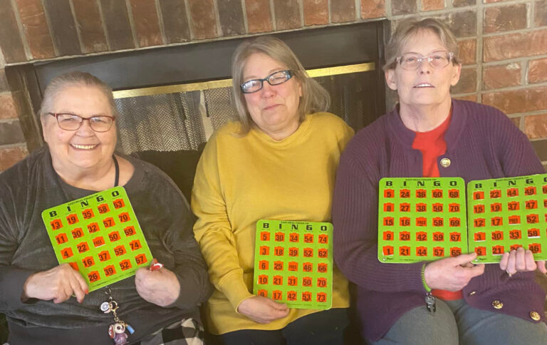 Three older adult women smile with their bingo cards at a senior living community in Greenwood, IN.